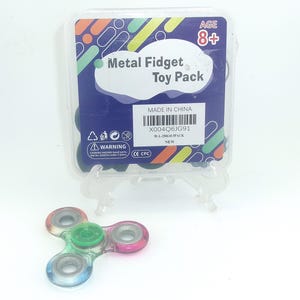 May include: A clear plastic case containing a Metal Fidget Toy Pack, suitable for ages 8+. A colorful fidget spinner with blue, green, and pink accents sits in front of the case. The case has a warning label and the text "MADE IN CHINA".