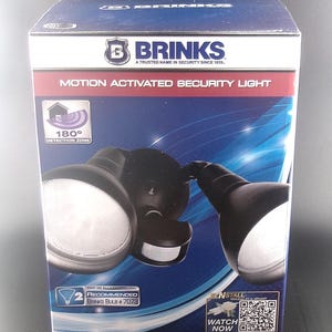May include: A box for a Brinks motion-activated security light. The box is blue and features a graphic of the light fixture with two round lights and a motion sensor. Text on the box includes "180° Detection Zone" and "Watch Now".