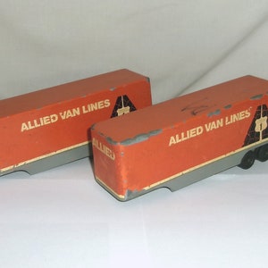 May include: Two orange toy semi-trailer trucks with the words "Allied Van Lines" printed on the side. The trucks have a gray bottom and black wheels.