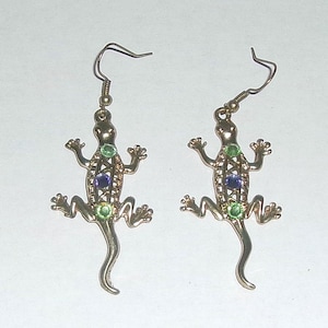 May include: A pair of gold-tone earrings featuring a lizard design with green and purple gemstones.