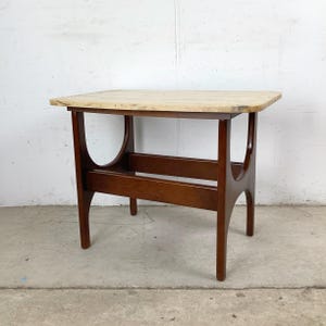 May include: A mid-century modern side table with a light-colored rectangular top and dark brown wooden legs. The legs have a curved design, and the table has a shelf. The table is approximately 24 inches long, 18 inches wide, and 20 inches high.