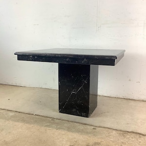 May include: A black marble side table with a square top and a rectangular pedestal base. The table has white veining throughout the black marble. The table is approximately 30 inches long, 30 inches wide, and 24 inches tall.