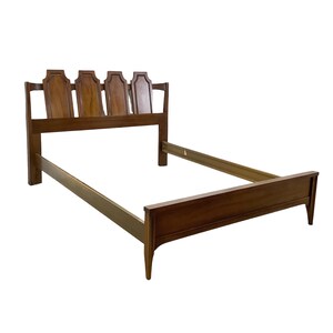 May include: A brown wooden bed frame featuring a headboard with four distinct, arched, raised panels. The frame includes two side rails and a low footboard with tapered legs, showcasing a smooth, polished finish throughout the entire structure.