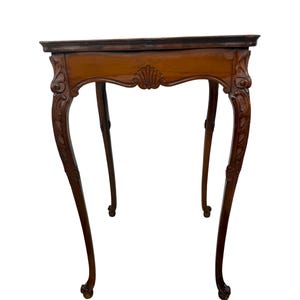 May include: A brown wooden side table featuring a rectangular top and four curved cabriole legs. The apron is decorated with carved shell motifs at the center and intricate scrollwork details at the top of each leg, ending in small feet.