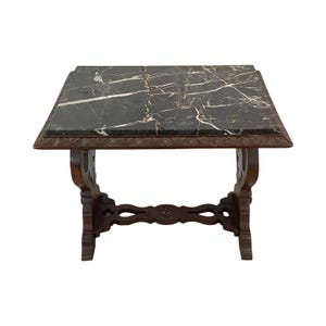 May include: A square, dark marble-topped table with a carved wooden base. The marble has white veining. The table's legs are intricately carved with decorative patterns. The table is a dark brown color and is likely an antique or vintage piece.