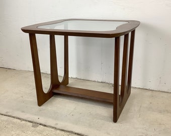 May include: A mid-century modern side table with a glass top and a unique, curved wooden frame. The table is made of dark wood and has a simple, elegant design.