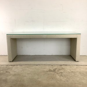 May include: A long, rectangular concrete console table with a clear glass top. The table has a modern, minimalist design and is perfect for a living room or entryway.
