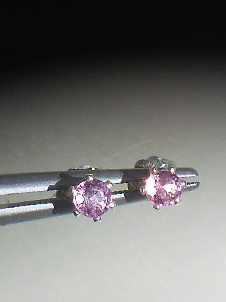 Pode incluir: Um par de brincos de prata com pequenas pedras preciosas cor-de-rosa.