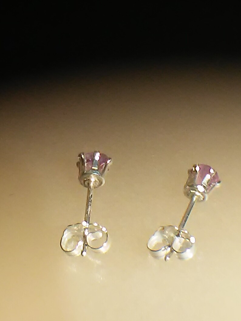 Pode incluir: Um par de brincos de prata com pequenas pedras preciosas cor-de-rosa.