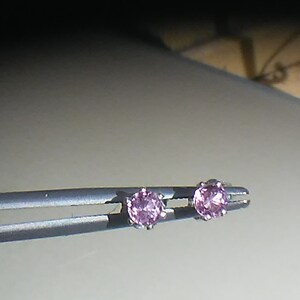Pode incluir: Um par de brincos de prata com pedras preciosas cor-de-rosa.