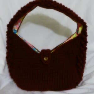 May include: A brown crocheted handbag with a floral fabric lining. The bag has a single button closure and a rounded shape.
