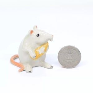 以下が含まれることがあります： トウモロコシを持ったネズミの白いセラミック製置物。置物はアメリカの25セント硬貨と同じくらいの大きさです。