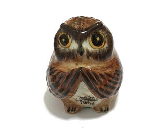 Könnte beinhalten: Eine kleine Keramik-Eulenfigur mit braunen und weißen Markierungen. Die Eule hat große, runde, gelbe Augen und einen ernsten Ausdruck.