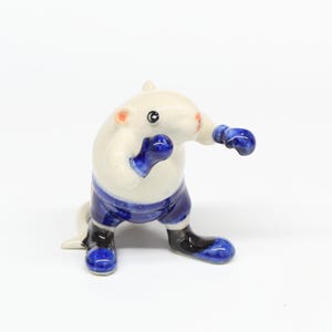 以下が含まれることがあります： 青いボクシンググローブと青いショートパンツを着用したボクシングラットの白いセラミック製フィギュア。