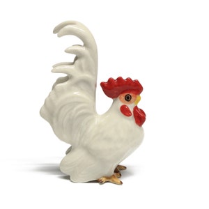 Peut inclure: Figurines de coq en céramique blanche avec une crête et des barbillons rouges. Le coq a une queue détaillée et se tient sur un fond blanc.
