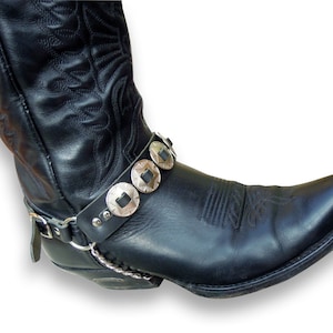May include: Black leather cowboy boot with a silver chain and a silver buckle strap with decorative round metal accents.