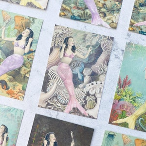 May include: A set of vintage postcards featuring illustrations of mermaids in various underwater scenes. The mermaids are depicted with long flowing hair, wearing seashells and holding mirrors. The postcards are printed on thick cardstock and have a slightly textured surface.