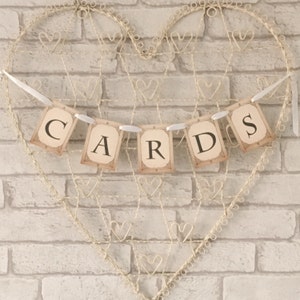 May include: A white banner with the word "CARDS" printed on it in black letters. The banner is strung on a wire heart-shaped frame against a brick wall.