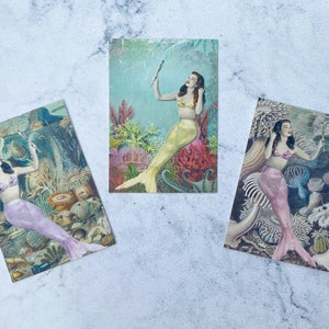 May include: Three vintage postcards featuring mermaids with colorful tails and underwater scenes. The mermaids are depicted with long flowing hair and are surrounded by coral, seaweed, and other marine life.
