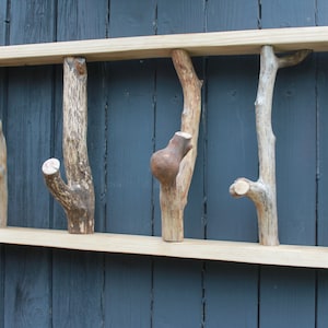 Op de afbeelding: Een houten wandbevestigde kapstok met vijf natuurlijke takken die uit het frame steken. De takken zijn van verschillende grootte en vorm, en ze zijn allemaal afgewerkt in een natuurlijke houtkleur.