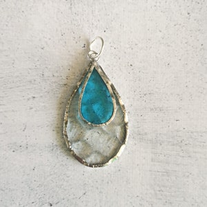May include: A teardrop-shaped pendant with a silver frame and a turquoise blue glass insert.