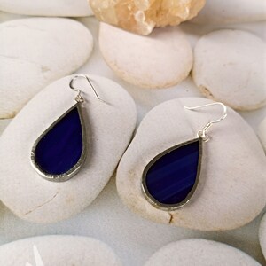 May include: A pair of teardrop-shaped earrings with a silver frame and a dark blue glass center.