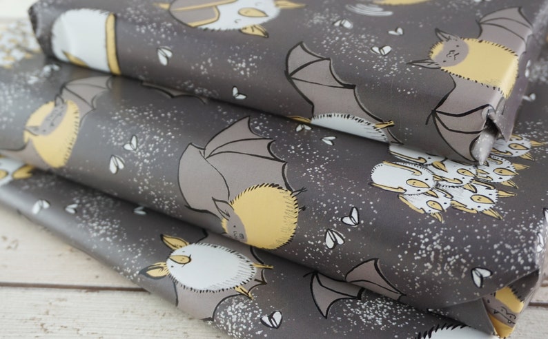 Op de afbeelding: Grijs cadeaupapier met een herhalend patroon van cartoonvleermuizen in grijs, geel en wit. De vleermuizen worden in verschillende poses getoond, met uitgespreide of gevouwen vleugels. Kleine witte, op insecten lijkende vormen zijn verspreid over de achtergrond.