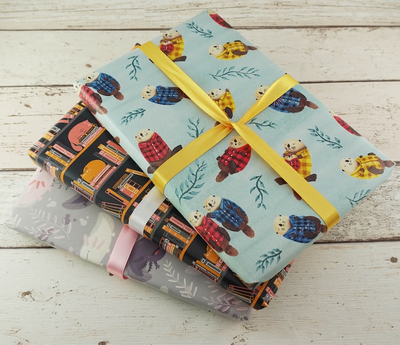 May include: Three wrapped gifts with patterned paper. One has a light blue background with otter illustrations wearing plaid shirts, tied with a yellow ribbon. Another has a black background with cat and book illustrations. The third has a gray background with floral illustrations.