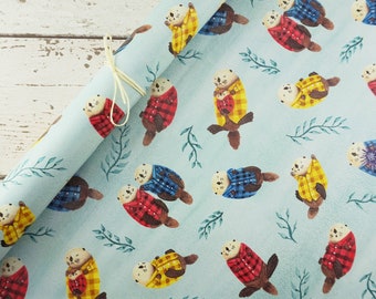 Op de afbeelding: Lichtblauw cadeaupapier met een herhaald patroon van otters in rood, geel en blauw geruite shirts. De otters zijn omgeven door groene takjes. Een crèmekleurig lint is om het opgerolde papier gebonden.