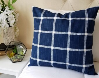 May include: A navy blue throw pillow with a white plaid pattern. The pillow is sitting on a white bed with a tufted headboard.