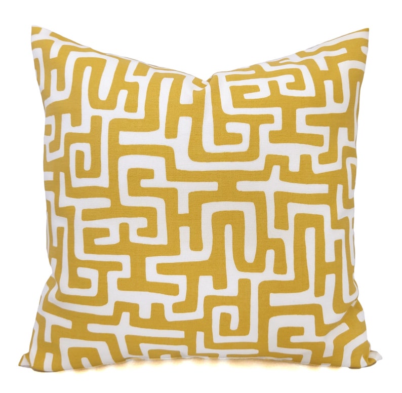 May include: Square decorative pillow with a mustard yellow and white geometric pattern. The pillow features a repeating maze-like design, creating a modern and stylish look. The pillow is a square shape, perfect for adding a pop of color and pattern to any room.