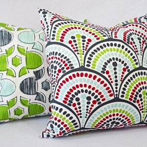 May include: Two decorative throw pillows with geometric patterns. One pillow features a red, green, and blue pattern with a white background. The other pillow features a black, white, red, and green pattern with a white background.