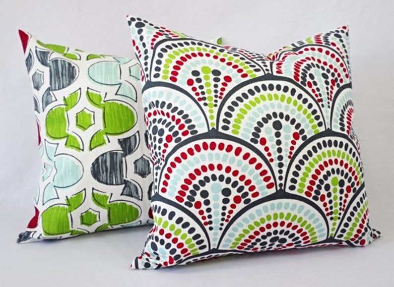 May include: Two decorative throw pillows with geometric patterns. One pillow features a red, green, and blue pattern with a white background. The other pillow features a black, white, red, and green pattern with a white background.