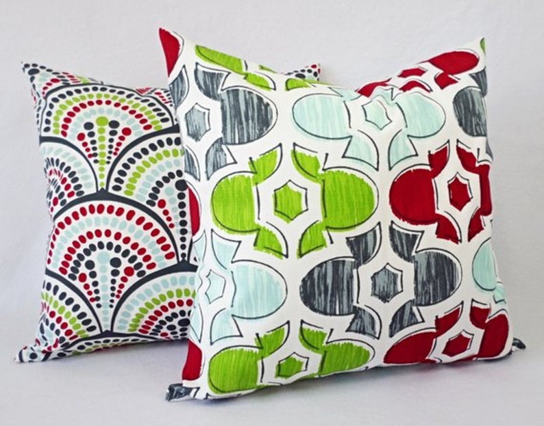May include: Two decorative throw pillows with geometric patterns. One pillow features a red, green, and blue pattern with a white background. The other pillow features a white, gray, and red pattern with a green background.