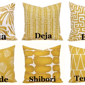 May include: Six decorative throw pillows in various patterns and designs. The pillows are primarily mustard yellow with white accents. Each pillow has a different pattern, including floral, geometric, and abstract designs. The names "Aria", "Deja", "Enid", "Shade", "Shibori", and "Terrain" are printed on the pillows.