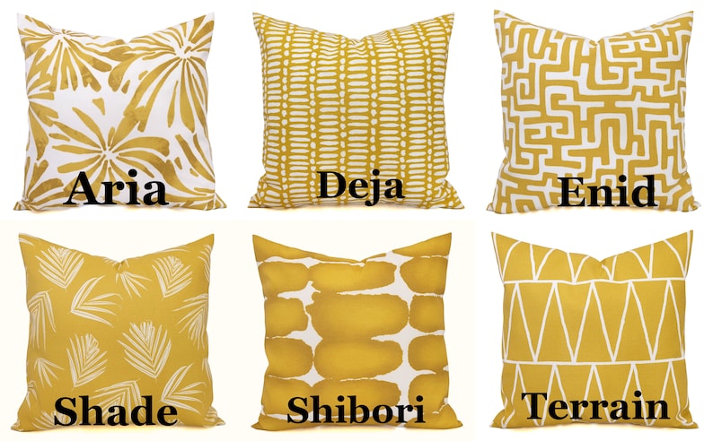 May include: Six decorative throw pillows in various patterns and designs. The pillows are primarily mustard yellow with white accents. Each pillow has a different pattern, including floral, geometric, and abstract designs. The names "Aria", "Deja", "Enid", "Shade", "Shibori", and "Terrain" are printed on the pillows.