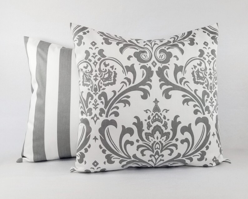 Pode incluir: Duas almofadas decorativas, uma com fundo branco e um padr&atilde;o damasco cinza, e a outra com listras brancas e cinzas.