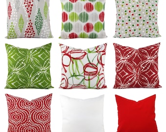 May include: A collection of nine square throw cushions featuring various patterns and colours. Designs include red and green geometric shapes, polka dots, abstract circles, and solid red and white covers. The cushions are arranged in a three-by-three grid.