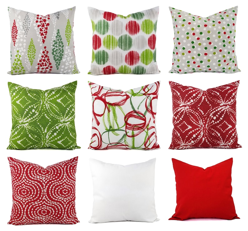 May include: A collection of nine square throw pillows featuring various patterns and colors. Designs include red and green geometric shapes, polka dots, abstract circles, and solid red and white covers. The pillows are arranged in a three-by-three grid.