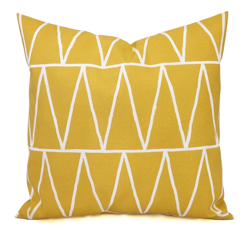 May include: Mustard yellow throw pillow with a geometric white triangle pattern. The pillow is square-shaped and has a textured appearance. The design is modern and suitable for home decor.