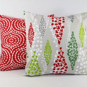May include: Two square throw pillows. The left pillow features a vibrant red background with a white dashed circular pattern. The right pillow has a light gray background with a vertical diamond-shaped pattern composed of red, green, and white dots.