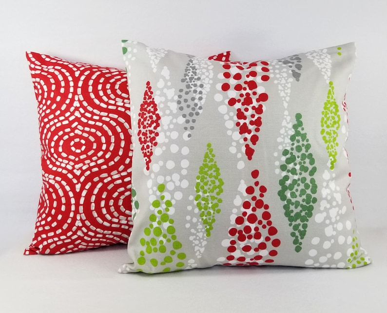 May include: Two square throw pillows. The left pillow features a vibrant red background with a white dashed circular pattern. The right pillow has a light gray background with a vertical diamond-shaped pattern composed of red, green, and white dots.