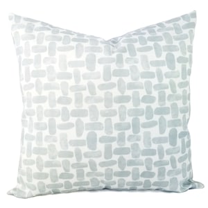 May include: A white throw pillow with a light blue geometric pattern. The pattern is made up of small, irregular shapes that resemble brushstrokes.