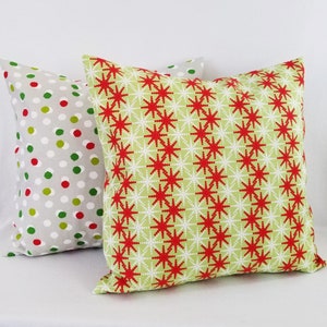 May include: Two decorative throw pillows with a Christmas theme. One pillow has a red and white snowflake pattern on a green background. The other pillow has a white background with red and green polka dots.