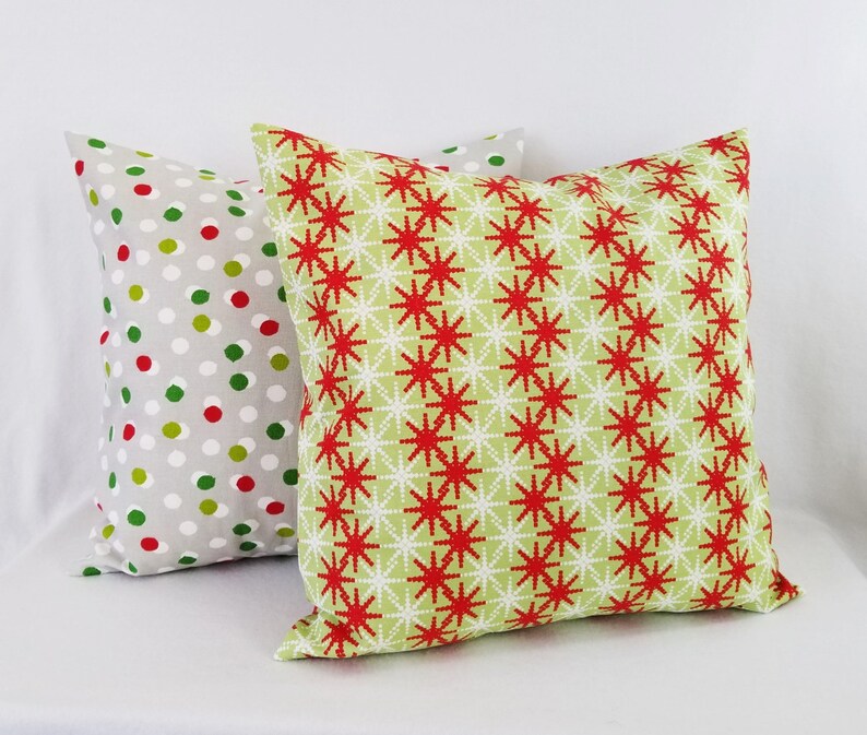 May include: Two decorative throw pillows with a Christmas theme. One pillow has a red and white snowflake pattern on a green background. The other pillow has a white background with red and green polka dots.