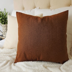May include: A brown throw pillow with a textured fabric surface. The pillow is sitting on a white faux fur blanket.