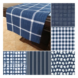 May include: A blue and white plaid table runner with a textured weave. The runner is on a dark wood table.