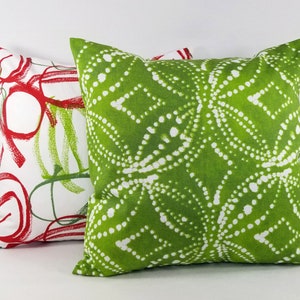 May include: Two square throw pillows. The front pillow features a vibrant lime green fabric with a white dotted geometric pattern. The back pillow is white with a bold red and green abstract circular and linear print design on the fabric.