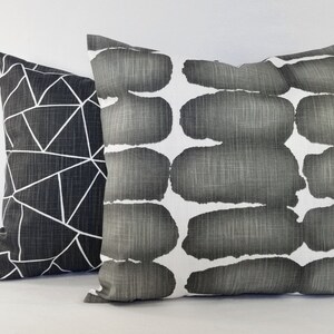 May include: Two square scatter cushions with a textured fabric finish. One cushion features a black background with a white geometric line pattern. The second cushion displays a white background with horizontal rows of dark grey brushstroke shapes.