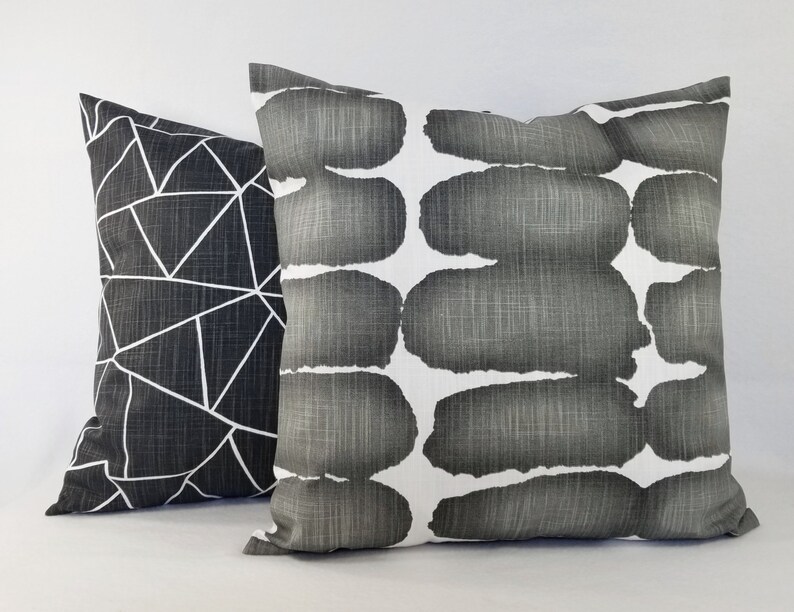 May include: Two square scatter cushions with a textured fabric finish. One cushion features a black background with a white geometric line pattern. The second cushion displays a white background with horizontal rows of dark grey brushstroke shapes.